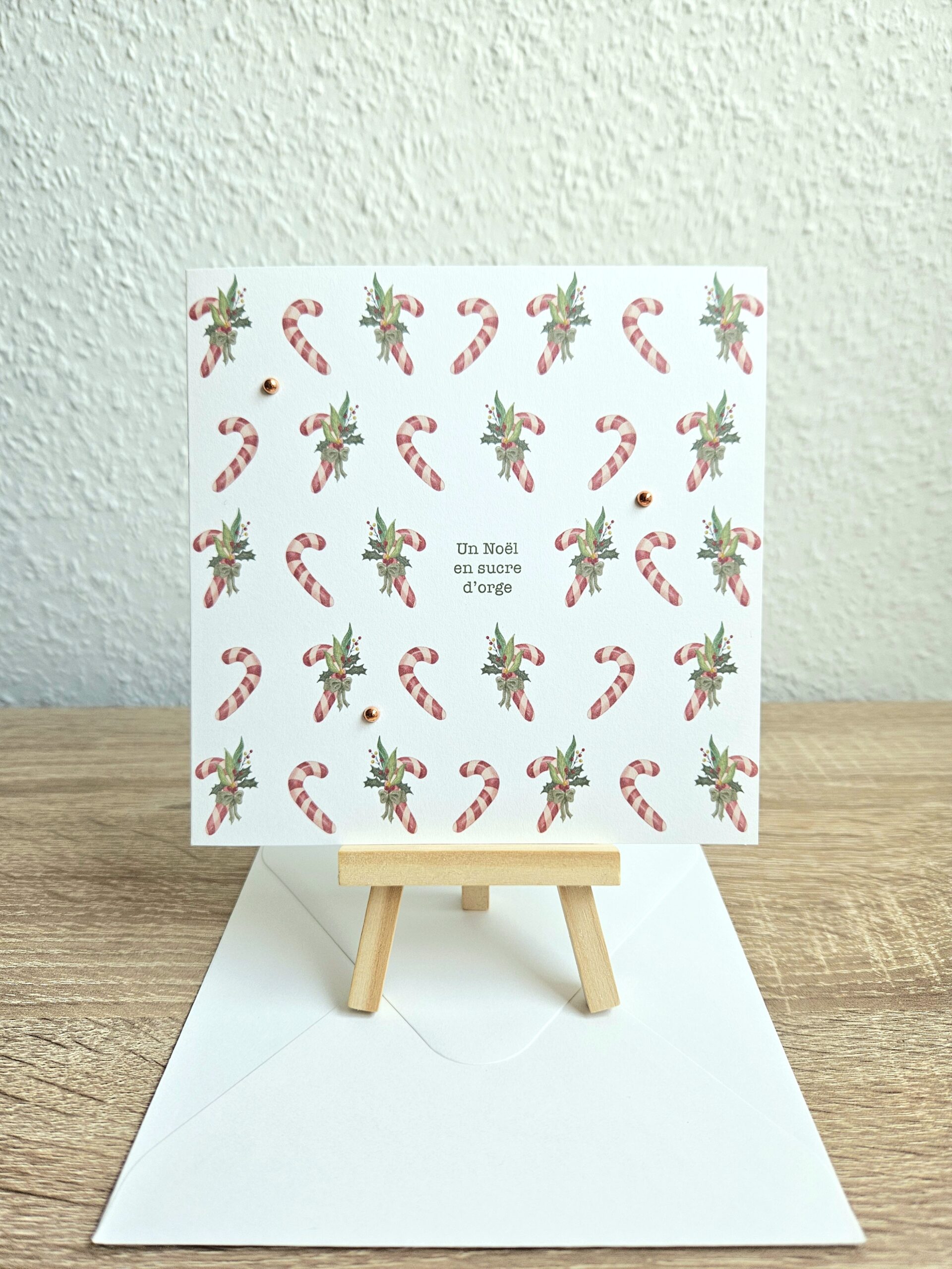 Carte de Noël "Un Noël en sucre d’orge" avec cannes en sucre et feuillage illustrés par @pyokoo_illustration, design Cartes d’émoi, décor doré, fabriquée à la main en Suisse