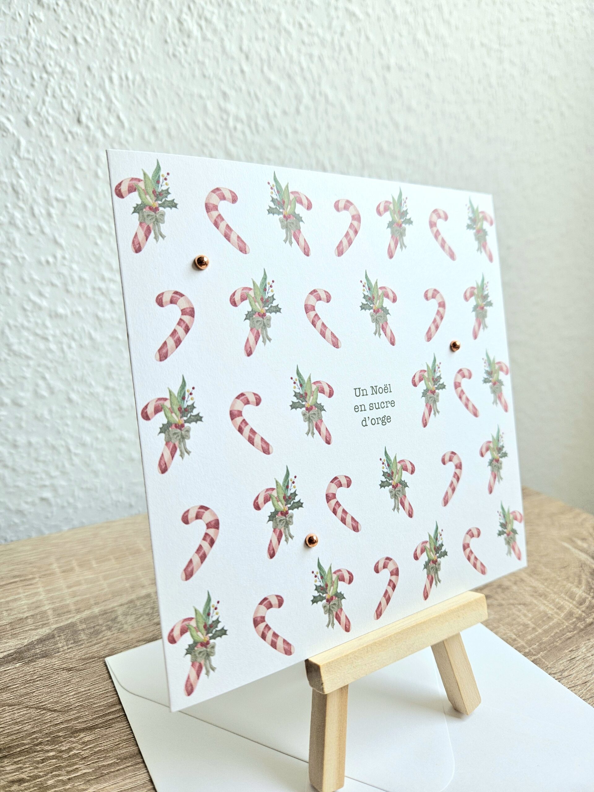 Carte de Noël "Un Noël en sucre d’orge" avec cannes en sucre et feuillage illustrés par @pyokoo_illustration, design Cartes d’émoi, décor doré, fabriquée à la main en Suisse