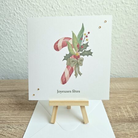 Carte de Noël artisanale "Joyeuses fêtes" avec canne en sucre et feuillage illustrés par @pyokoo_illustration, design Cartes d’émoi, décor doré, fabriquée à la main en Suisse