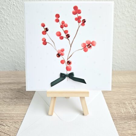 Carte de Noël illustrée avec une branche de baies rouges, strass et noeud vert, création artisanale Cartes d’émoi.