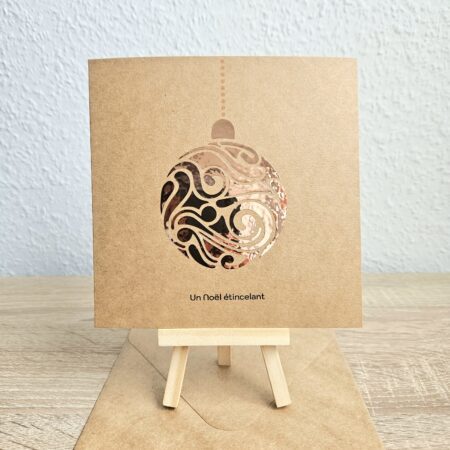 Carte de Noël en kraft avec une boule scintillante cuivrée découpée, message "Un Noël étincelant", création artisanale Cartes d’émoi.