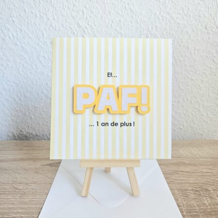 Carte d’anniversaire avec le message "Et… PAF ! 1 an de plus !" sur fond rayé jaune.