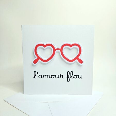 Carte blanche avec lunettes en forme de coeurs rouges et le message "L’amour flou".