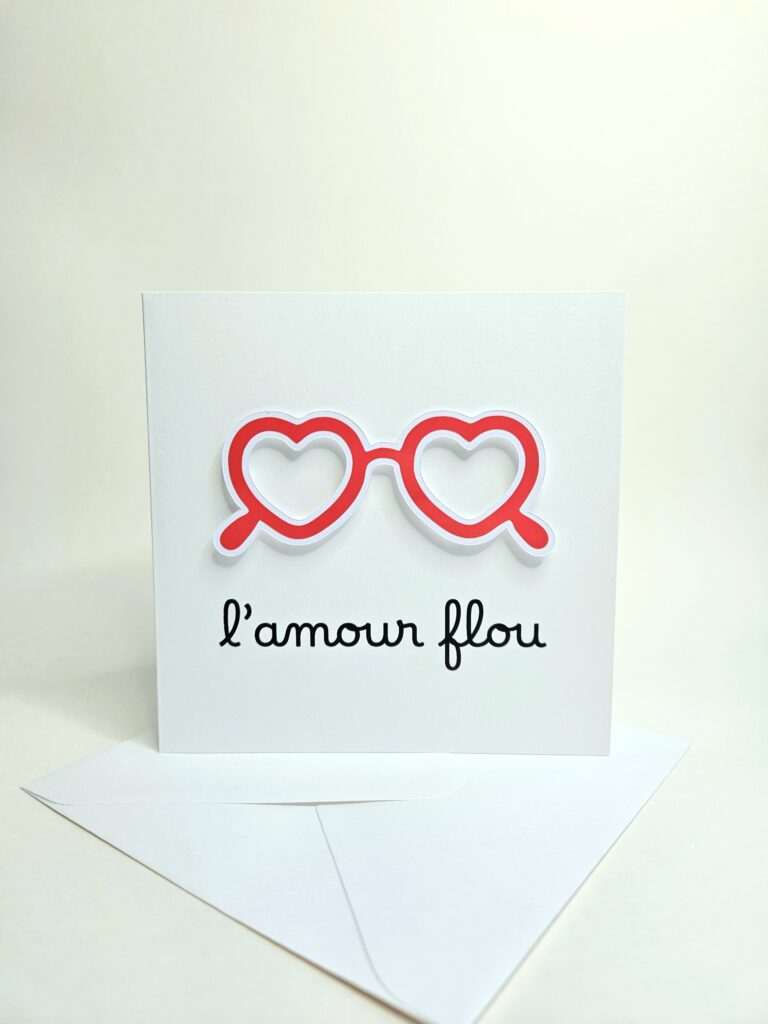 Carte blanche avec lunettes en forme de coeurs rouges et le message "L’amour flou".