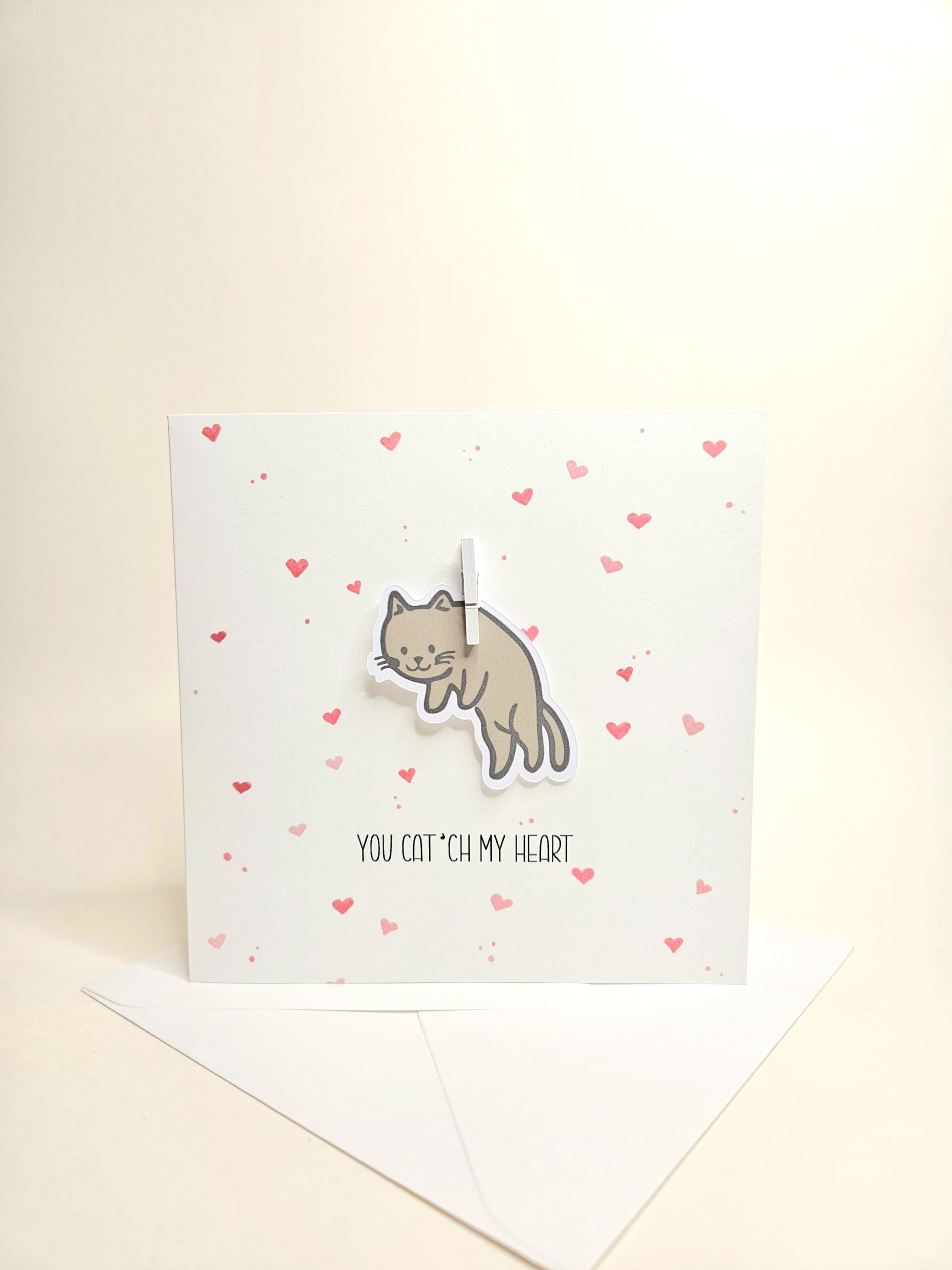 Carte d’amour avec illustration de chat et le texte "You cat’ch my heart", décorée de petits coeurs.