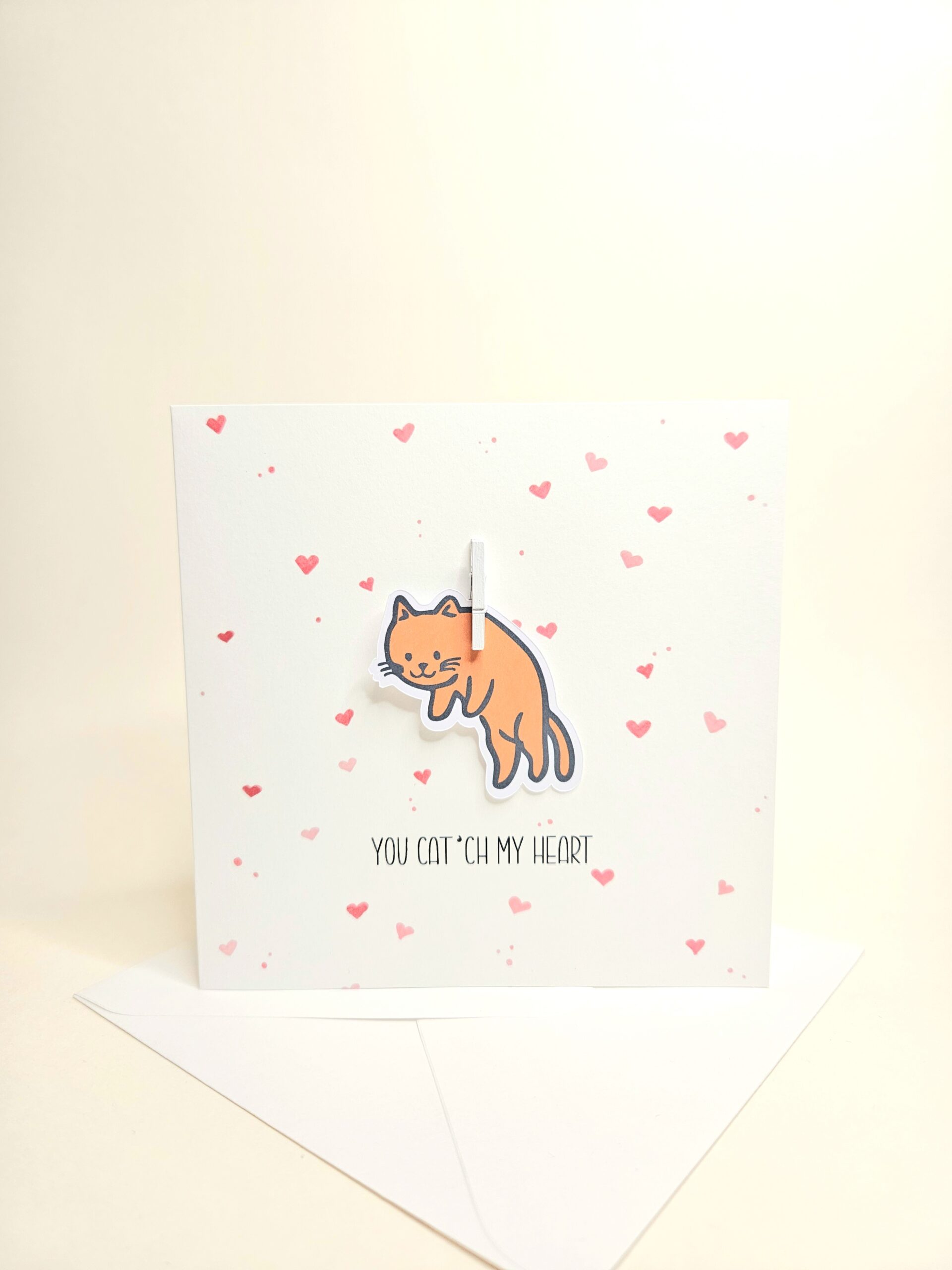 Carte d’amour avec illustration de chat et le texte "You cat’ch my heart", décorée de petits coeurs.
