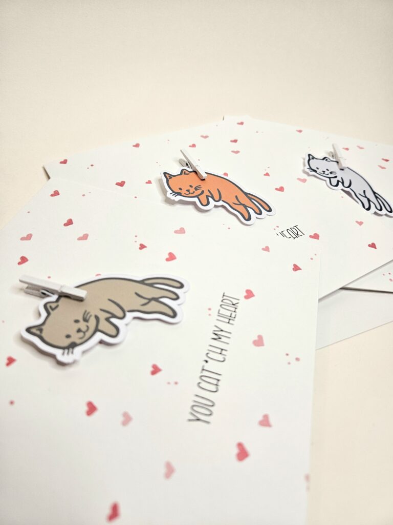 Carte d’amour avec illustration de chat et le texte "You cat’ch my heart", décorée de petits coeurs.