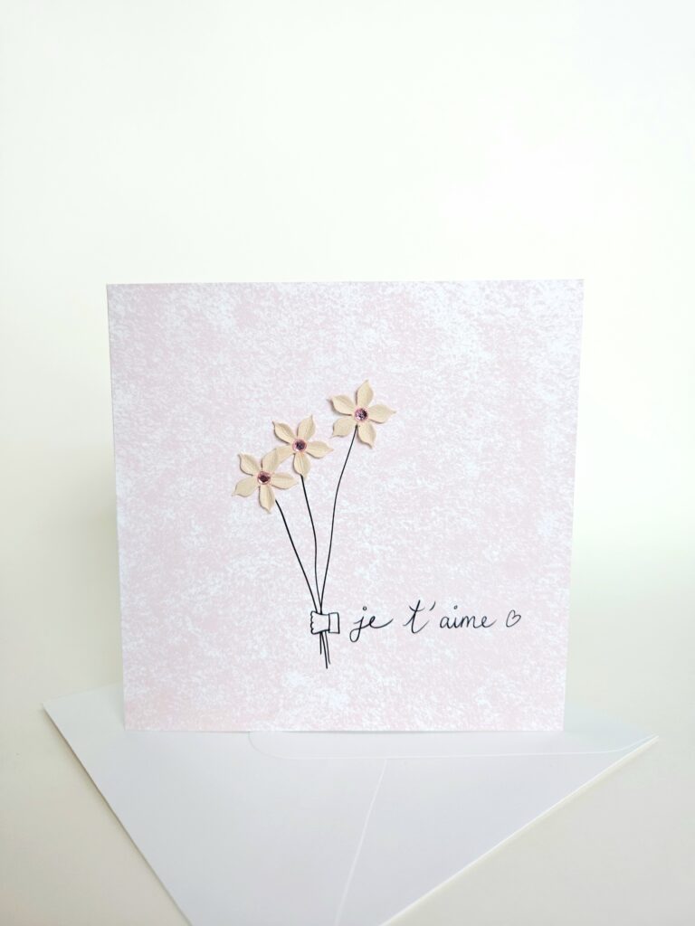 Carte d’amour rose avec bouquet de fleurs en relief et le message "je t’aime".