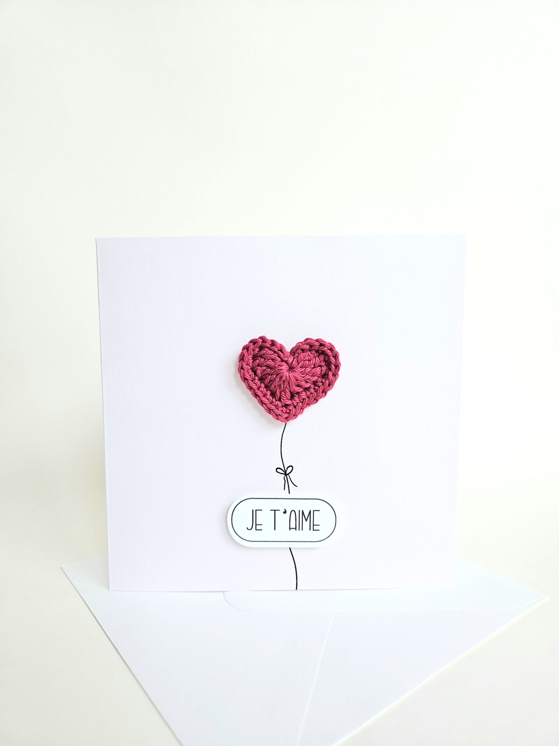 Carte d’amour minimaliste avec coeur rouge bordeaux crocheté à la main en forme de ballon et message "je t’aime", coeur magnet détachable.