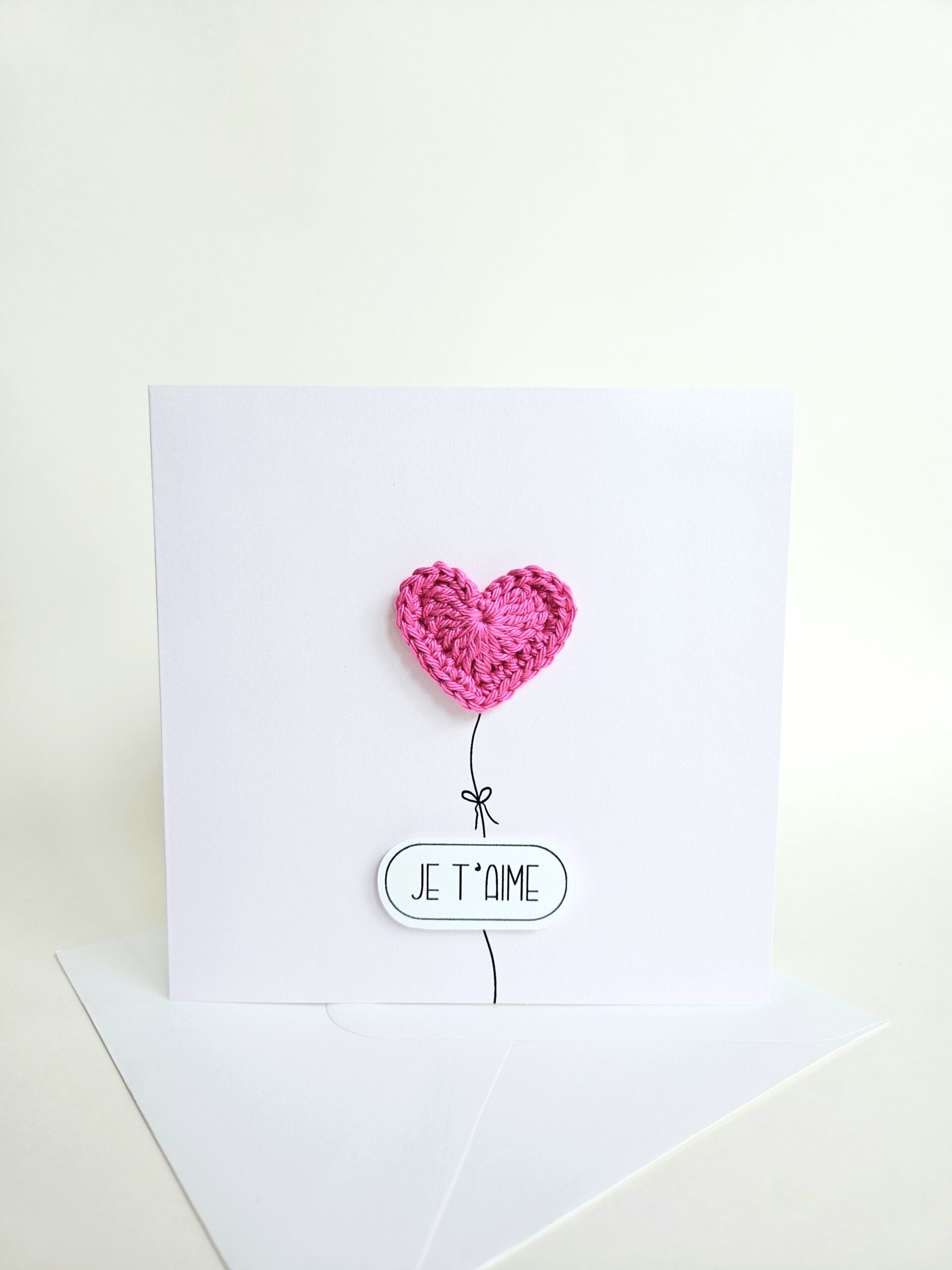 Carte d’amour minimaliste avec coeur rose fuchsia crocheté à la main en forme de ballon et message "je t’aime", coeur magnet détachable.