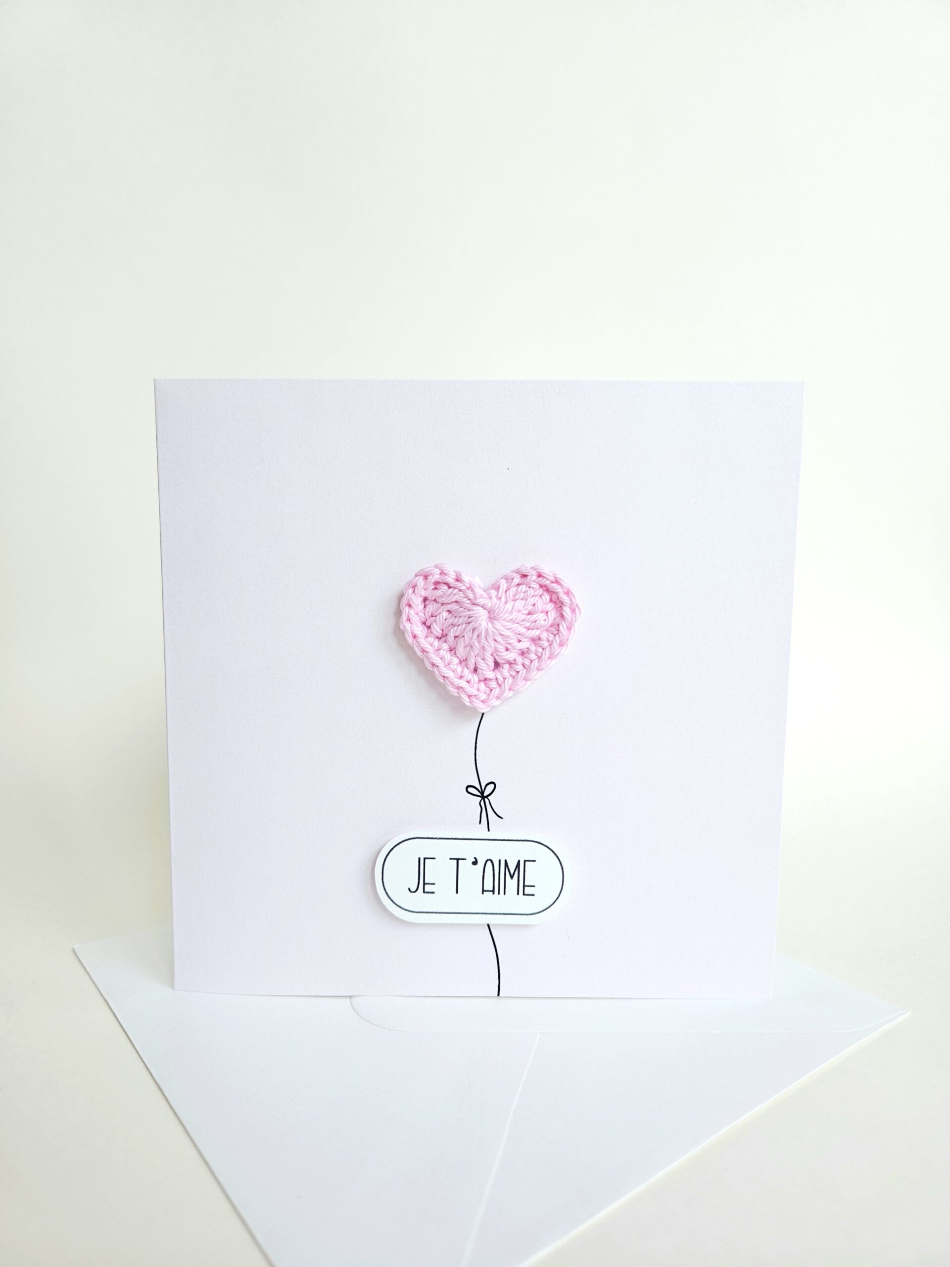 Carte d’amour minimaliste avec coeur rose clair crocheté à la main en forme de ballon et message "je t’aime", coeur magnet détachable.