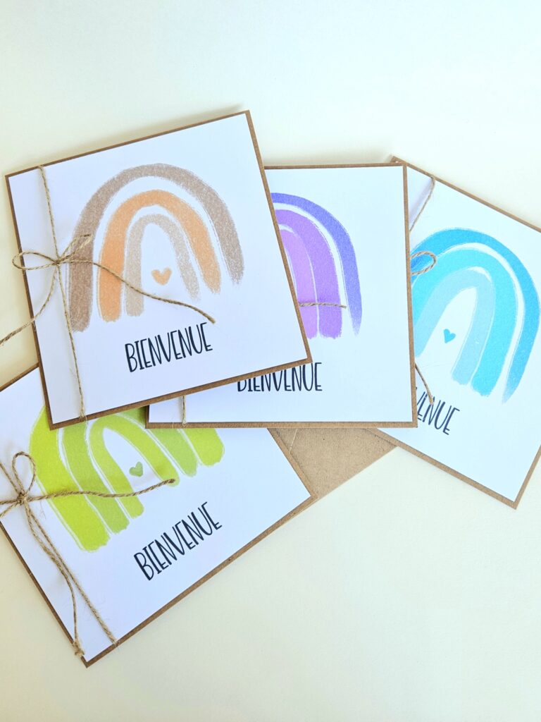 Carte de naissance avec arc-en-ciel minimaliste et le message "Bienvenue", attachée avec une ficelle naturelle.
