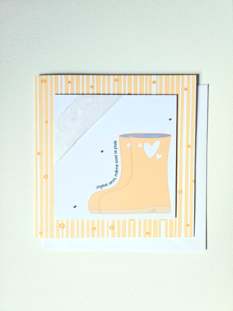 Carte d’anniversaire automne avec une botte jaune décorée de petits coeurs sur fond rayé.